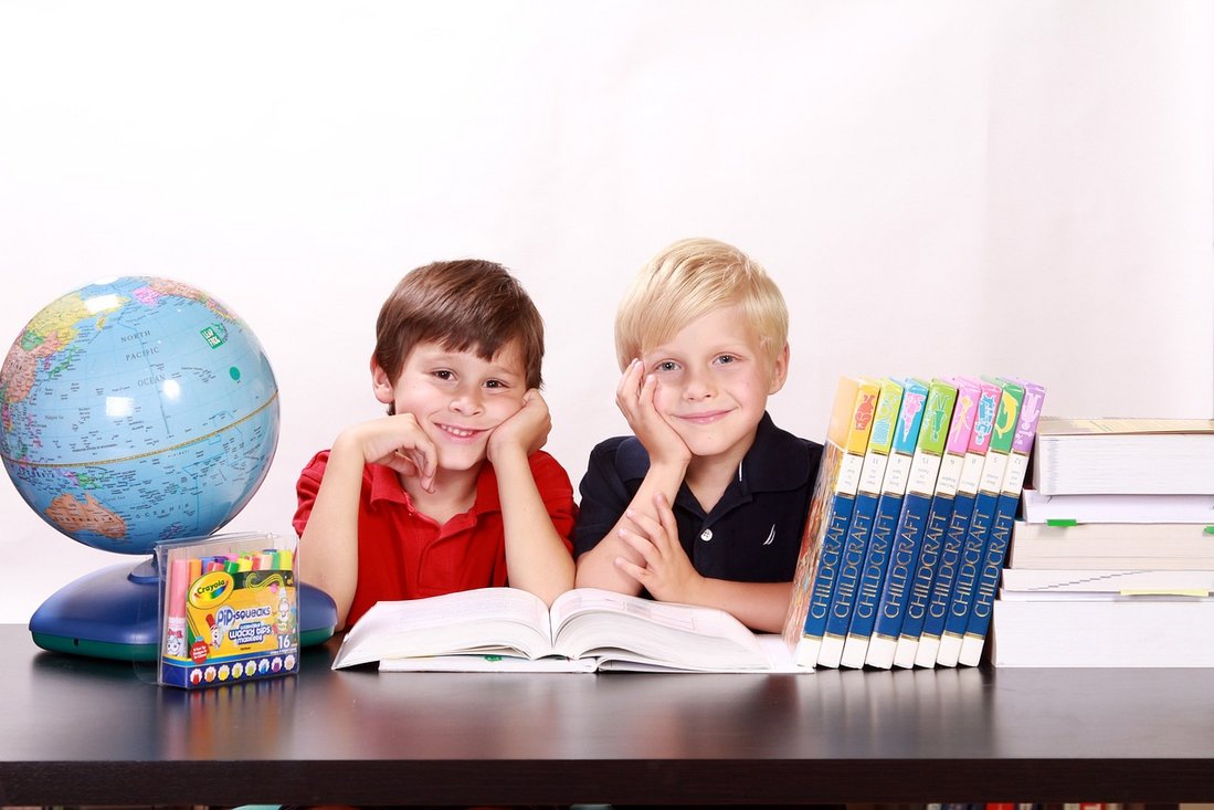 Zwei Jungen sitzen lächelnd am Tisch, auf dem ein Globus und Bücher liegen. Kinder Bild. Frei zur Verwendung.Bild von Kris von Pixabay.