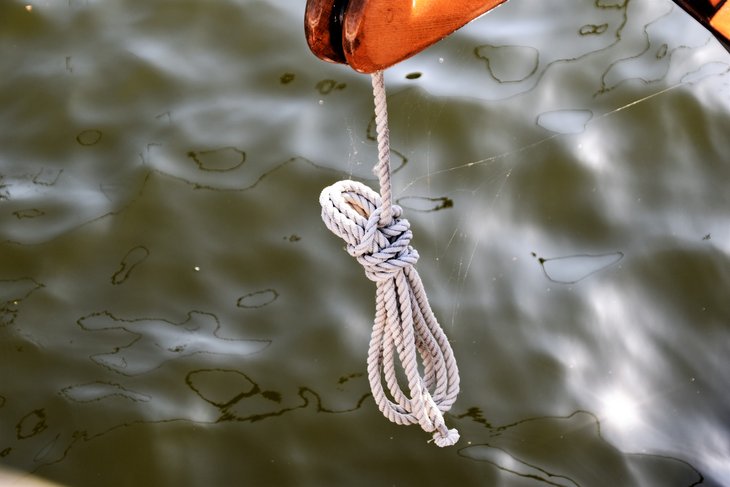 Seil an einem Segelboot hängt über einem Ölfilm auf dem Wasser.